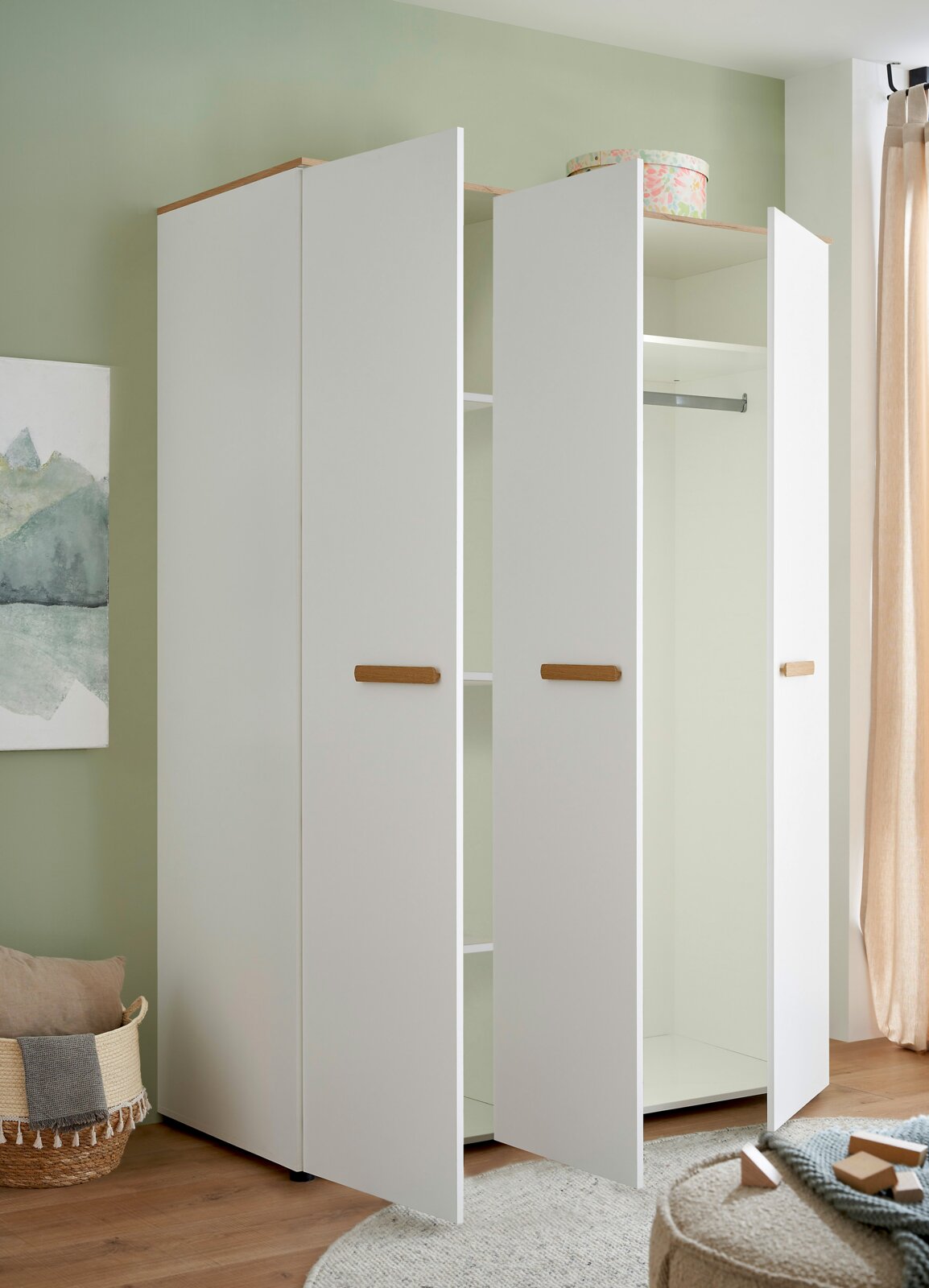 Weißer Kleiderschrank mit drei geöffneten Türen, Holzgriffen und Einlegeböden sowie Kleiderstange, fotografiert in leicht schräger Frontansicht im Raum