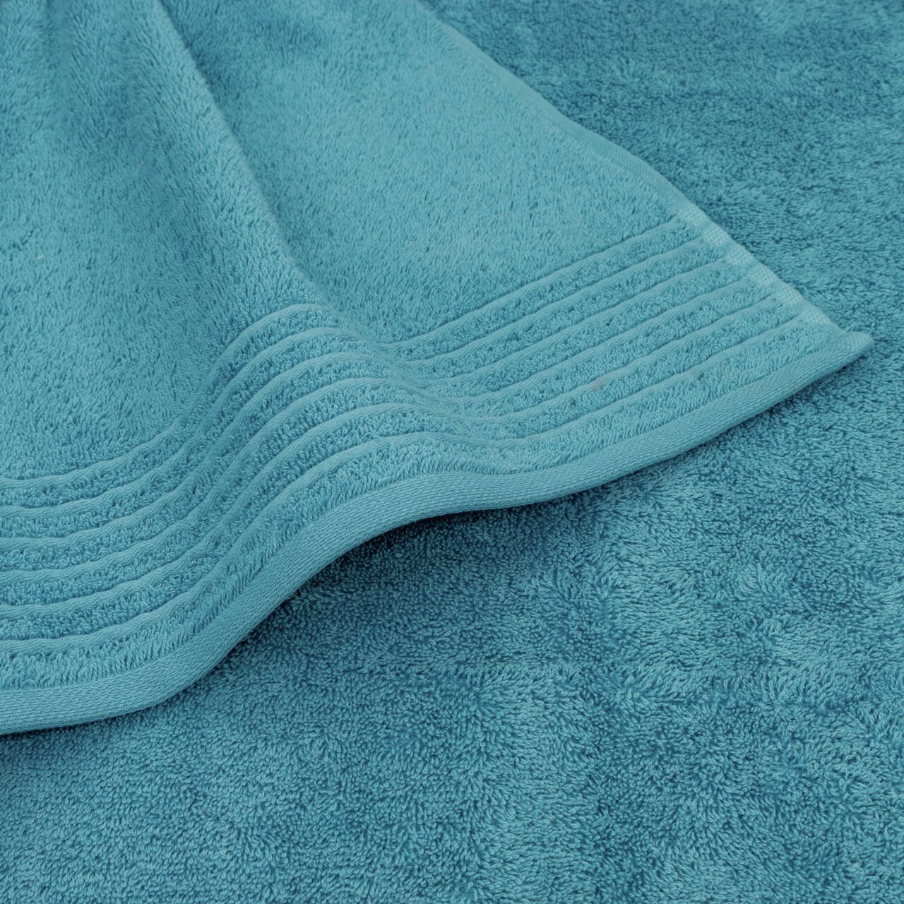 Close-up van een turquoise handdoek met decoratieve strepen aan de rand.