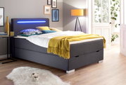 Modern boxbed met grijze stoffen bekleding, ledverlichting in het hoofdeinde en kleurrijke versieringen, zijaanzicht