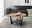 Runder Couchtisch aus Holz mit schwarzem Metallgestell und Glasablage, im Wohnzimmer mit grauem Sofa und dekorativen Kissen, aus seitlicher Perspektive.