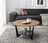Runder Couchtisch aus Holz mit schwarzem Metallgestell und Glasablage, im Wohnzimmer mit grauem Sofa und dekorativen Kissen, aus seitlicher Perspektive.