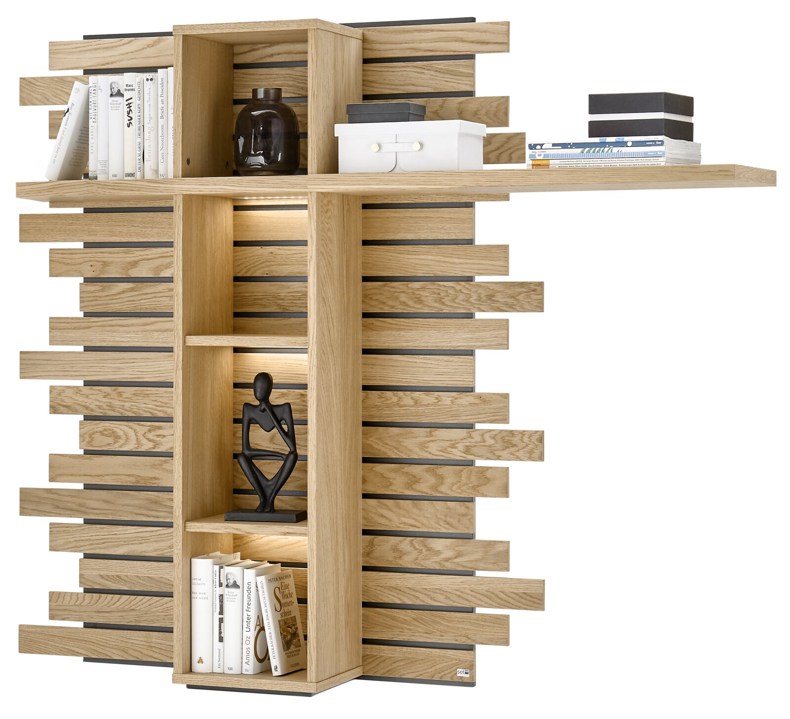 Set one by Musterring Hängepaneel SET ONE JACKSON Modernes Wandregal aus hellem Holz mit versetzt angeordneten Lamellen, integrierter Beleuchtung und Ablageflächen, bestückt mit Büchern und Deko; frontale Ansicht.