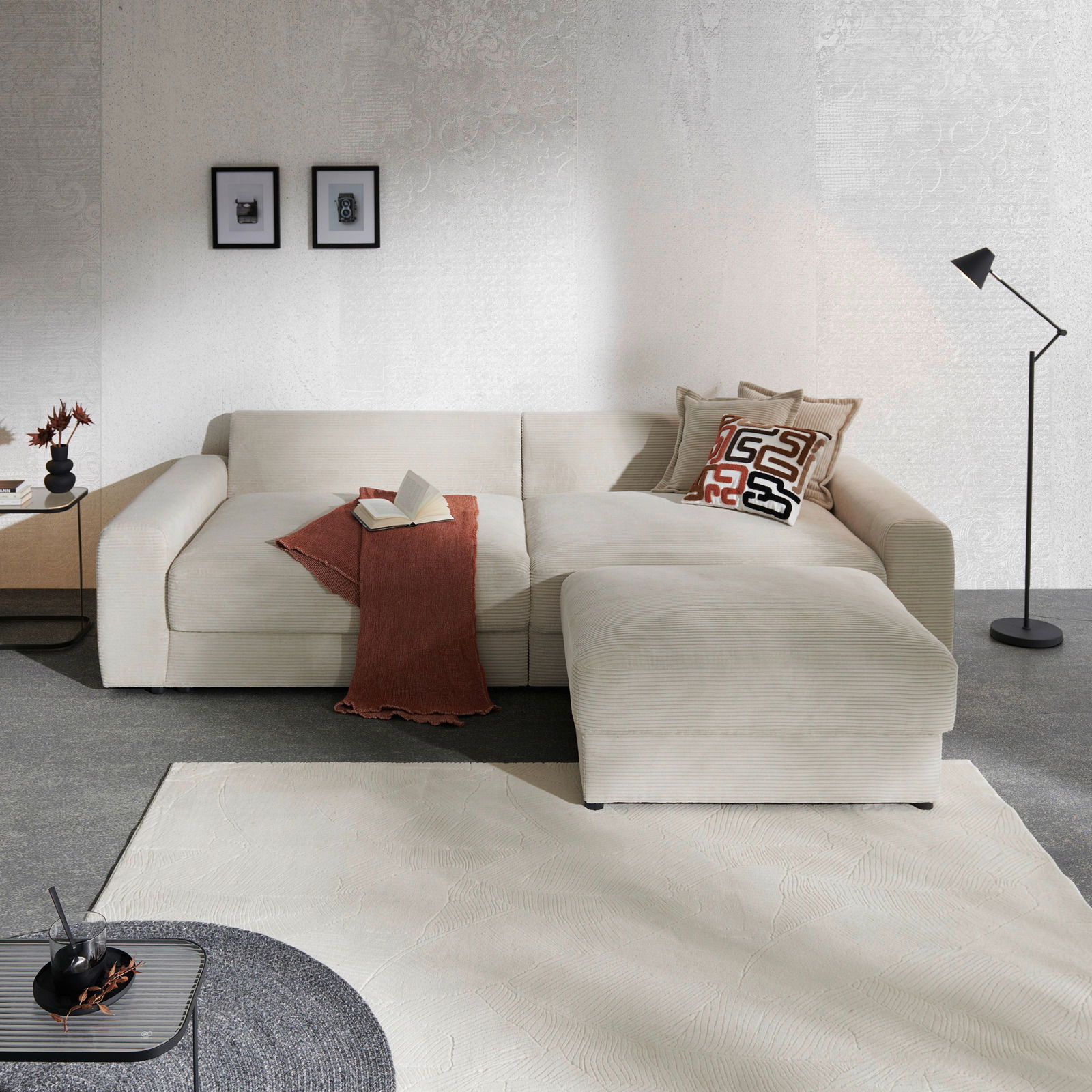 Großes, cremefarbenes Big-Sofa in einer modernen Wohnzimmerumgebung, von vorne betrachtet. Dekoriert mit Kissen und einer Decke, umgeben von stilvollen Accessoires.