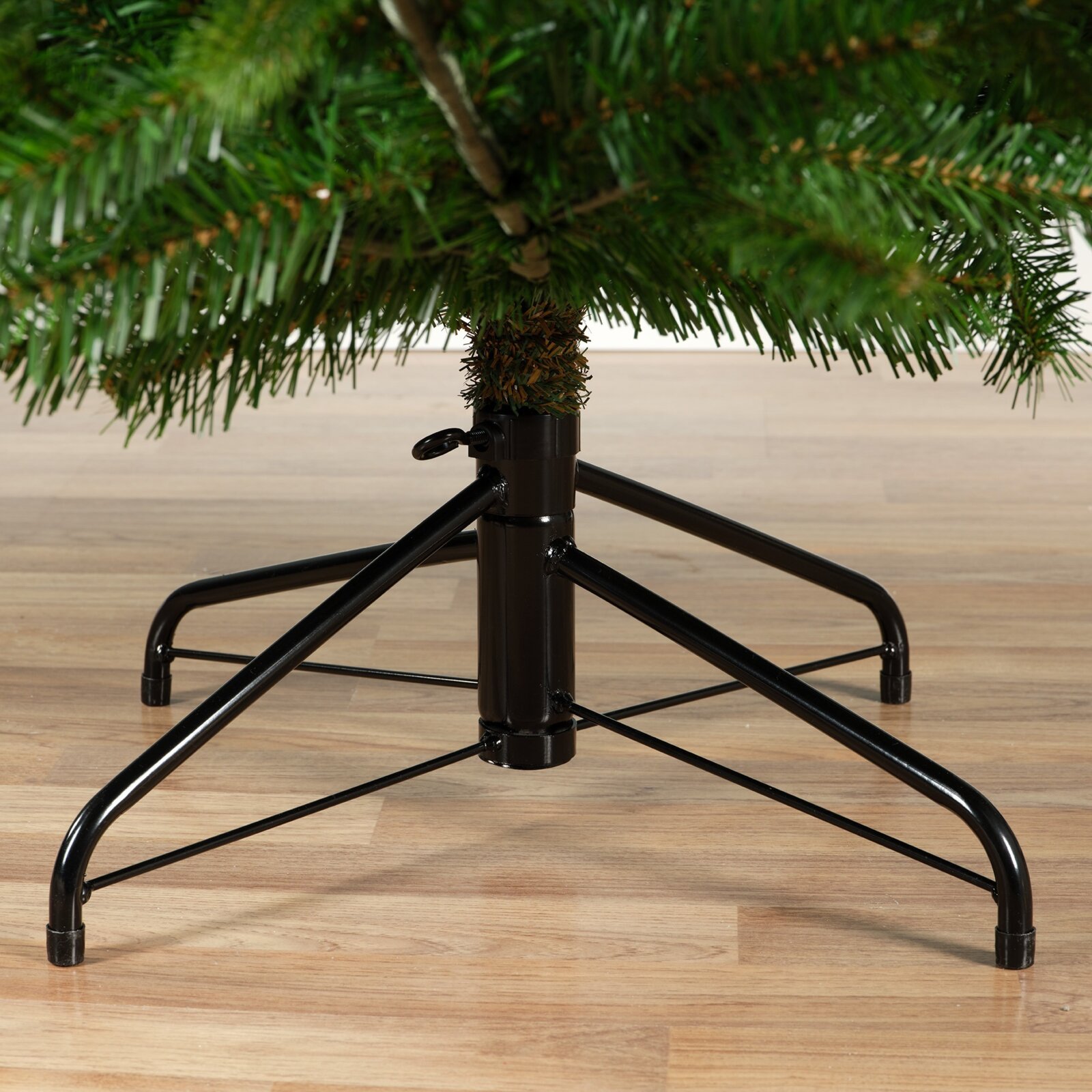 Nahaufnahme aus frontaler Perspektive auf den stabilen schwarzen Metallständer eines künstlichen Weihnachtsbaums mit ausladenden Standfüßen und Feststellschraube