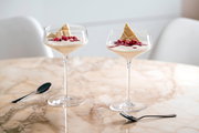 Zwei elegante Champagnerschalen mit Dessert, dekoriert mit weißer Schokolade und Granatapfelkernen, auf einem Marmortisch aus der Seitenperspektive.