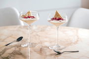 Zwei elegante Champagnerschalen mit Dessert, dekoriert mit weißer Schokolade und Granatapfelkernen, auf einem Marmortisch aus der Seitenperspektive.