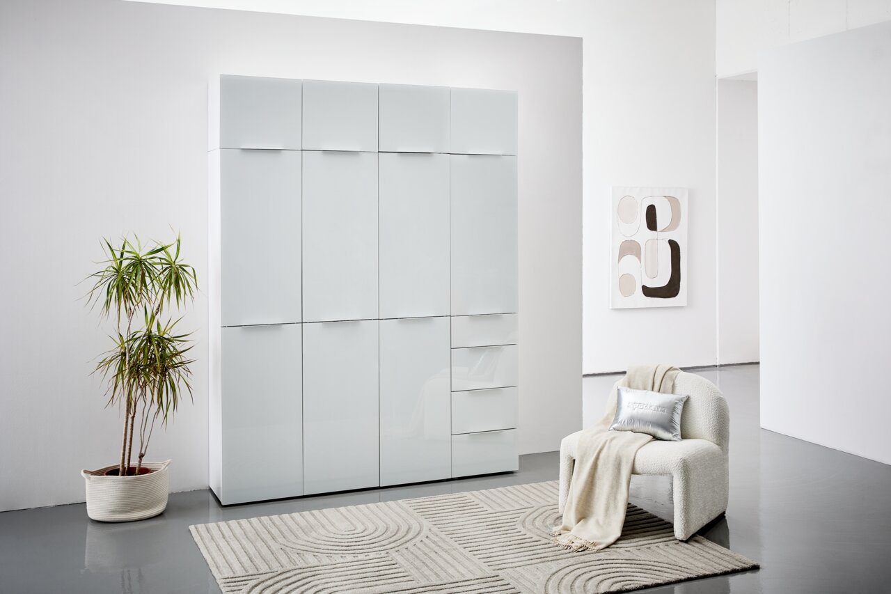 Voleo Mehrzweckschrank MALIN Moderner weißer Mehrzweckschrank mit Hochglanzoberfläche, frontal fotografiert, in einem stilvoll eingerichteten Raum mit Pflanze und Sessel.