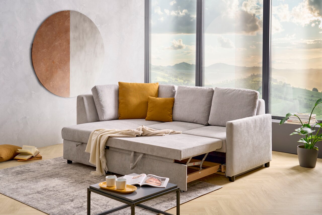 Graue Funktionsrundecke mit ausziehbarem Bett, dekoriert mit senfgelben Kissen, in einem modernen Wohnzimmer mit großem Fenster und Blick auf die Landschaft. Perspektive von vorne.