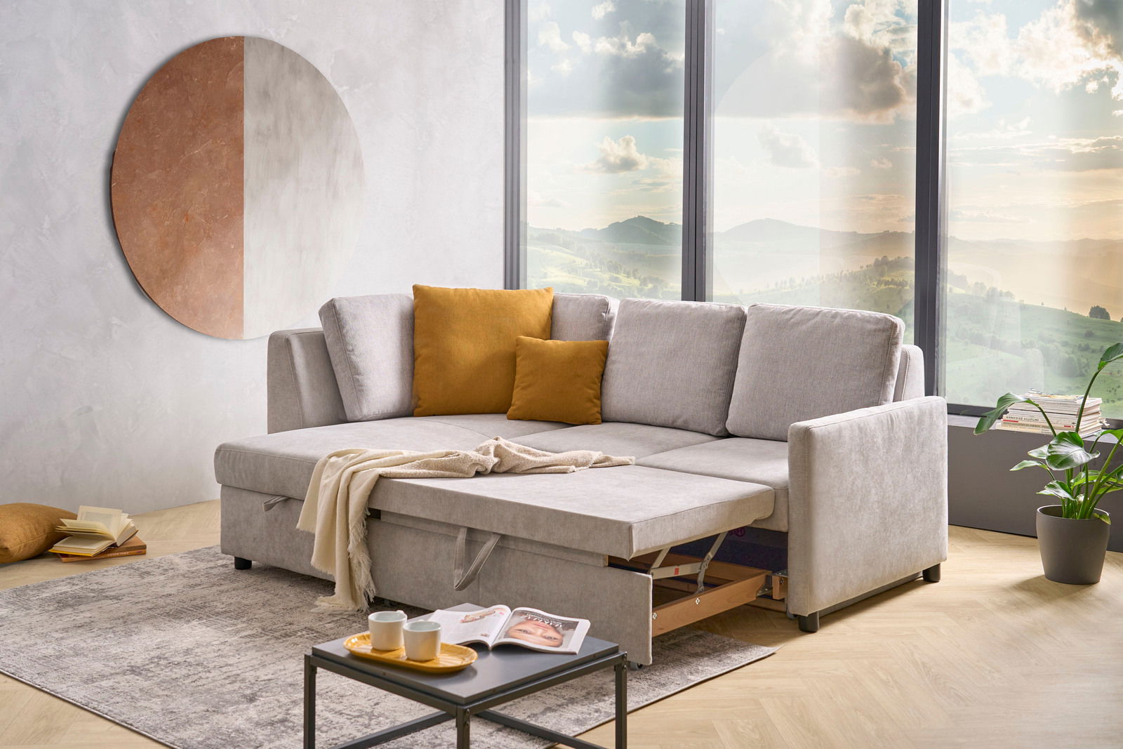 Graue Funktionsrundecke mit ausziehbarem Bett, dekoriert mit senfgelben Kissen, in einem modernen Wohnzimmer mit großem Fenster und Blick auf die Landschaft. Perspektive von vorne.