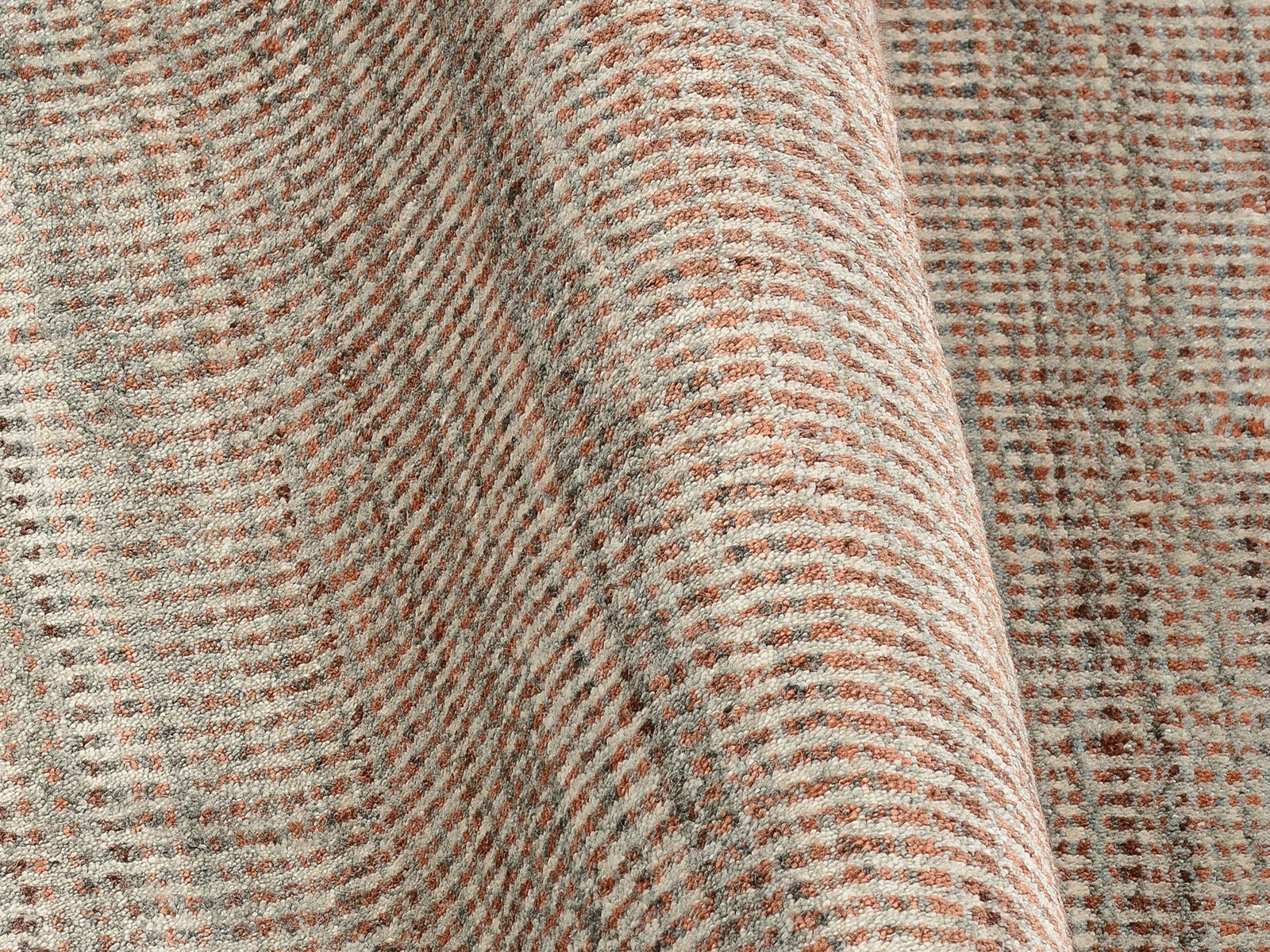 Nahaufnahme eines Designer Teppichs mit einem geometrischen Muster in Beige- und Brauntönen, perspektivisch von der Seite aufgenommen.