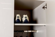 Offener weißer Kleiderschrank mit Einlegeboden und Kleiderstange; oben stehen zwei weiße Sportschuhe mit blauer Sohle, Frontansicht aus dem Schrankinneren