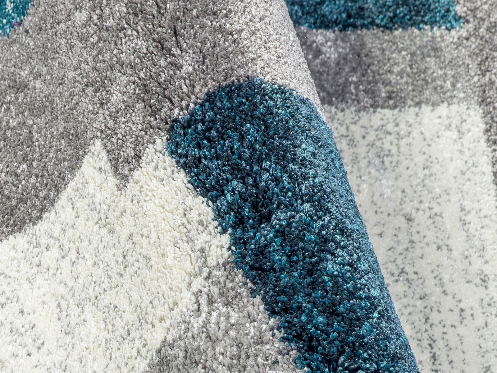 Nahaufnahme eines Frisé-Teppichs mit grauen, weißen und türkisfarbenen Mustern, perspektivisch von der Seite aufgenommen.