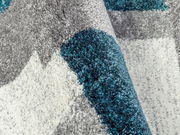 Nahaufnahme eines Frisé-Teppichs mit grauen, weißen und türkisfarbenen Mustern, perspektivisch von der Seite aufgenommen.