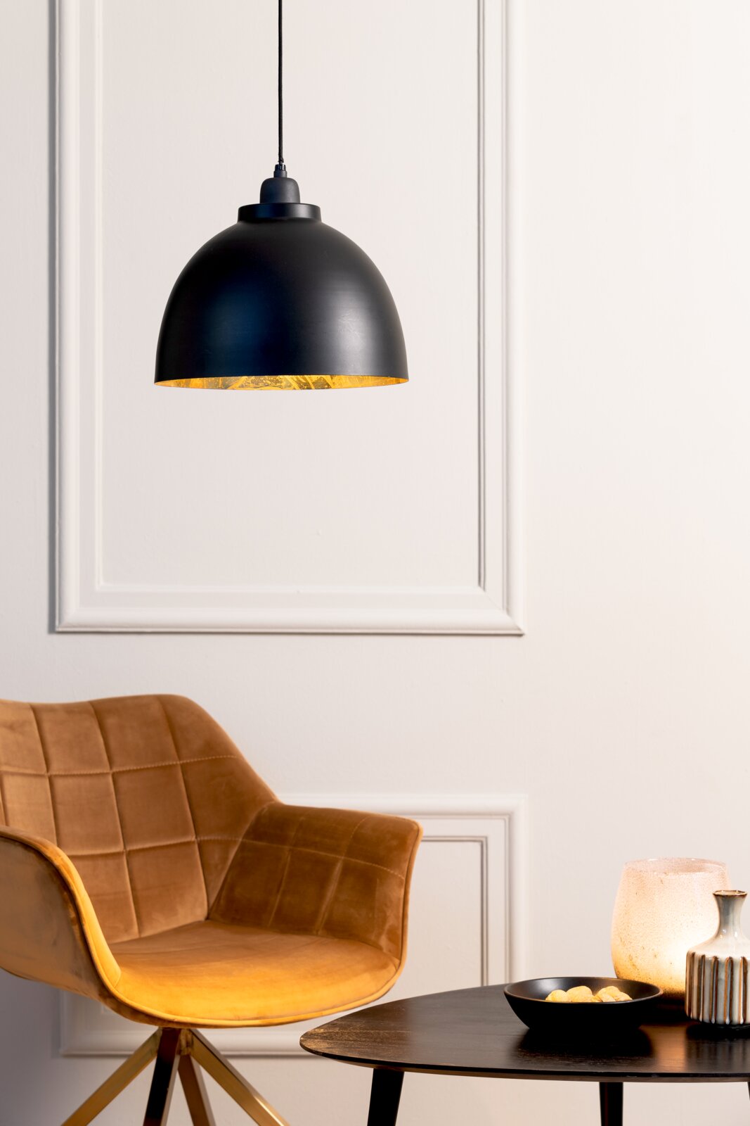 Schwarze Hängeleuchte mit goldener Innenseite, im modernen Wohnambiente mit braunem Sessel und Tisch, seitliche Perspektive