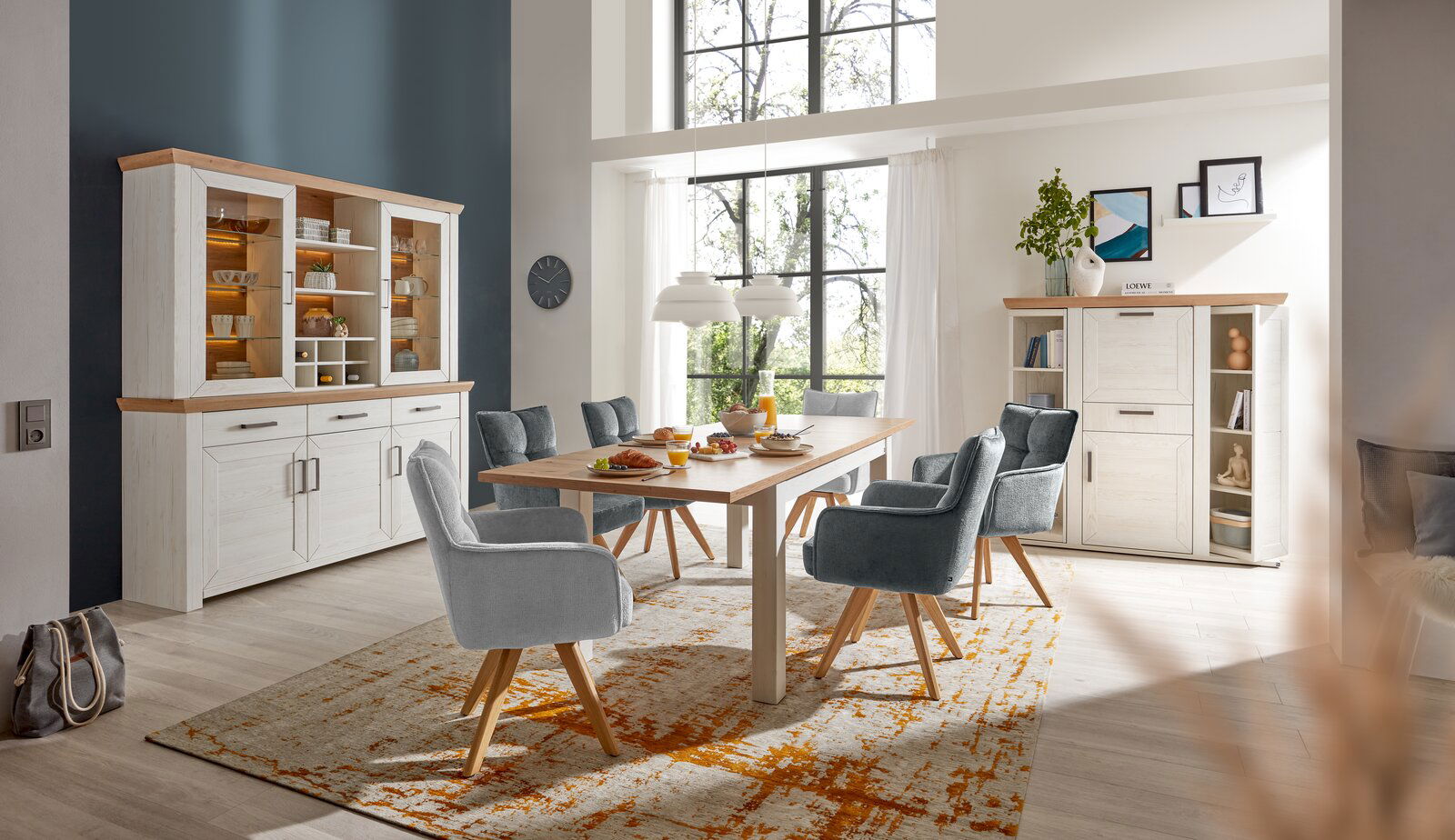 Set one by Musterring Armlehnstuhl SET ONE TUCSON Moderner Essbereich mit Armlehnstühlen in grauem Stoffbezug und Holzbeinen, um einen Holztisch arrangiert. Perspektive von der Seite.