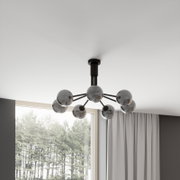 Moderne plafondlamp in Sputnik-stijl met een zwart metalen frame en zes rookgrijze glazen bollen, gefotografeerd vanuit een licht schuin perspectief vanuit de woonkamer, voor het raam en het gordijn.