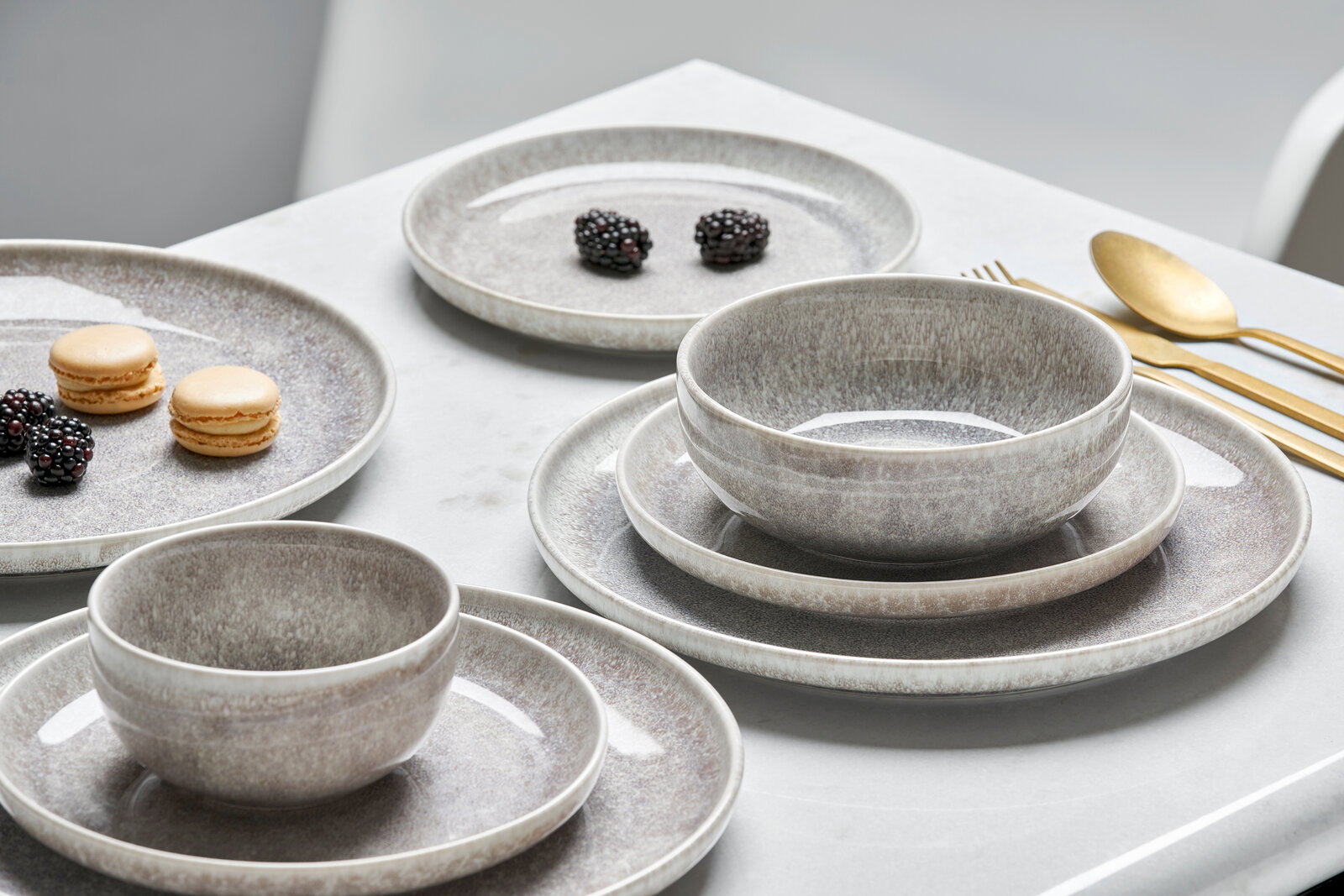 Elegantes 12-teiliges Tellerset in Grau mit Schalen und Tellern, seitliche Perspektive auf einem gedeckten Tisch mit goldfarbenem Besteck.