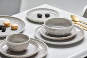 Elegantes 12-teiliges Tellerset in Grau mit Schalen und Tellern, seitliche Perspektive auf einem gedeckten Tisch mit goldfarbenem Besteck.
