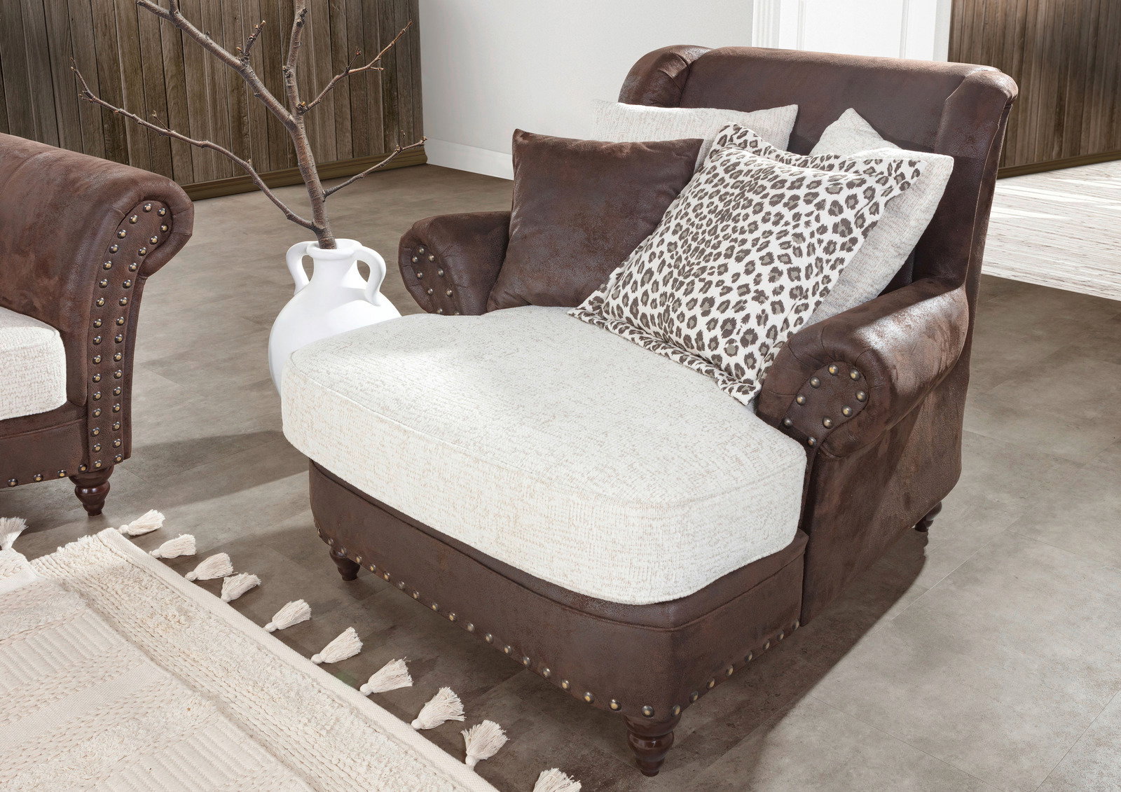 Grote, comfortabele fauteuil in bruine kunstleer met een lichte zitting en decoratieve kussens, gezien vanaf de zijkant.