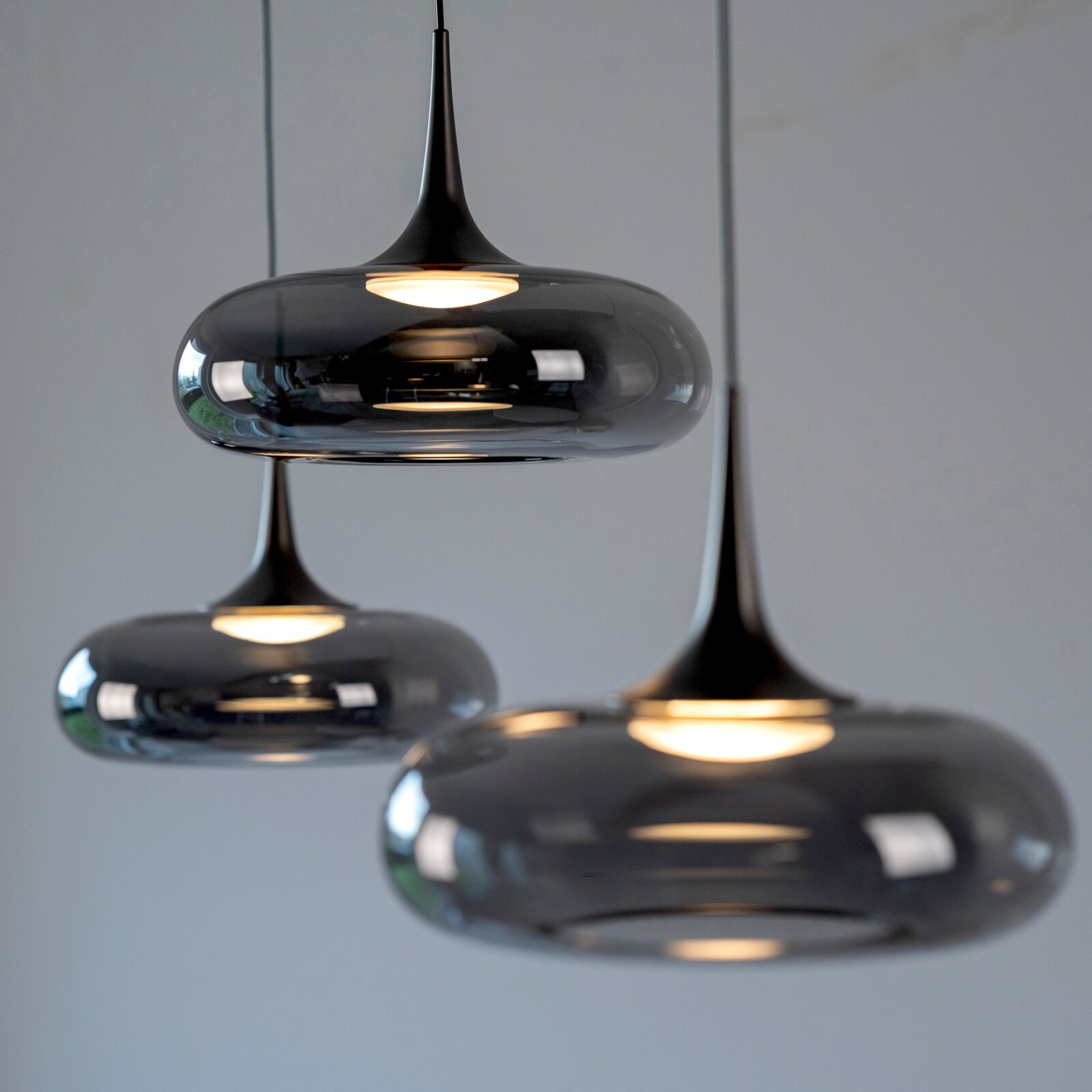 Moderne Pendelleuchten aus rauchgrauem Glas mit warmem Licht, hängend an schwarzen Kabeln, in schräger Nahaufnahme von vorn.