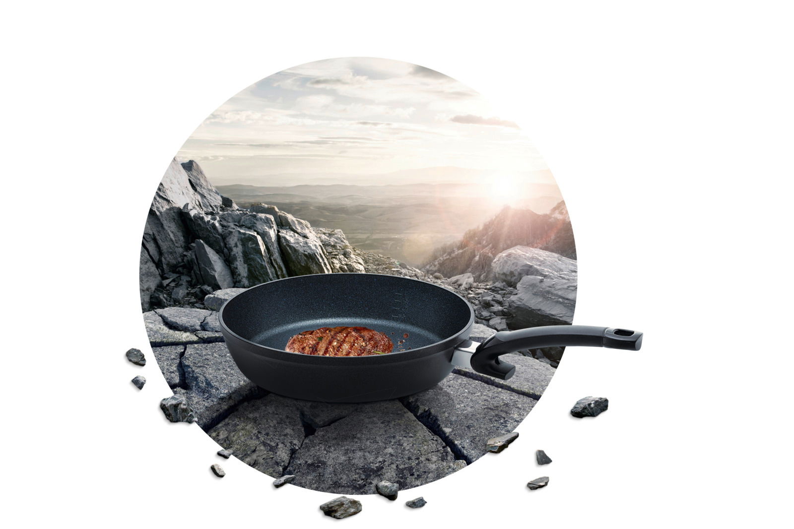 Pfanne Adamant Comfort mit gebratenem Steak, auf einem Felsen in einer Berglandschaft platziert, seitliche Perspektive.