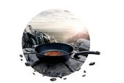 Pfanne Adamant Comfort mit gebratenem Steak, auf einem Felsen in einer Berglandschaft platziert, seitliche Perspektive.