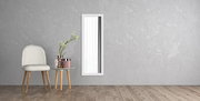 Rechteckiger Wandspiegel mit weißem Rahmen, vertikal an einer grauen Wand montiert, neben einem Stuhl und einem kleinen Tisch mit Dekorationen, aus seitlicher Perspektive.