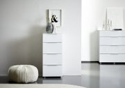 Weiße Hochkommode mit vier Schubladen, dekoriert mit einer Vase und Büchern, in einem modernen, minimalistischen Raum. Perspektive von vorne.