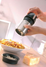 Hand hält eine universelle Käsereibe über einem Teller mit Pasta, seitliche Perspektive