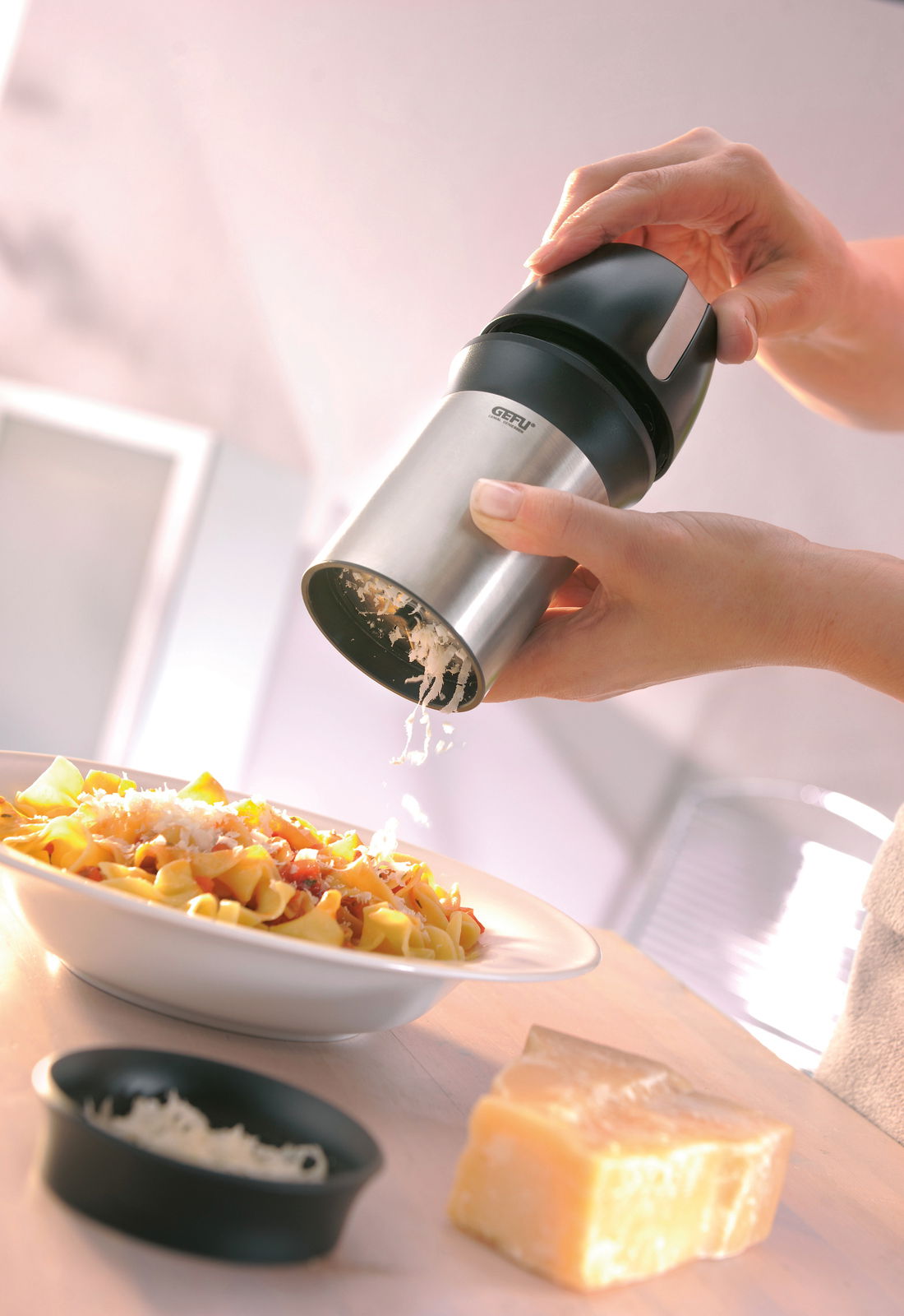 Hand hält eine universelle Käsereibe über einem Teller mit Pasta, seitliche Perspektive