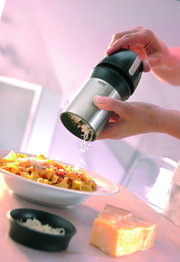 Hand hält eine universelle Käsereibe über einem Teller mit Pasta, seitliche Perspektive