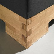 Detailansicht einer Ecke eines Boxspringbetts mit Holzverkleidung und dunklem Stoffbezug.