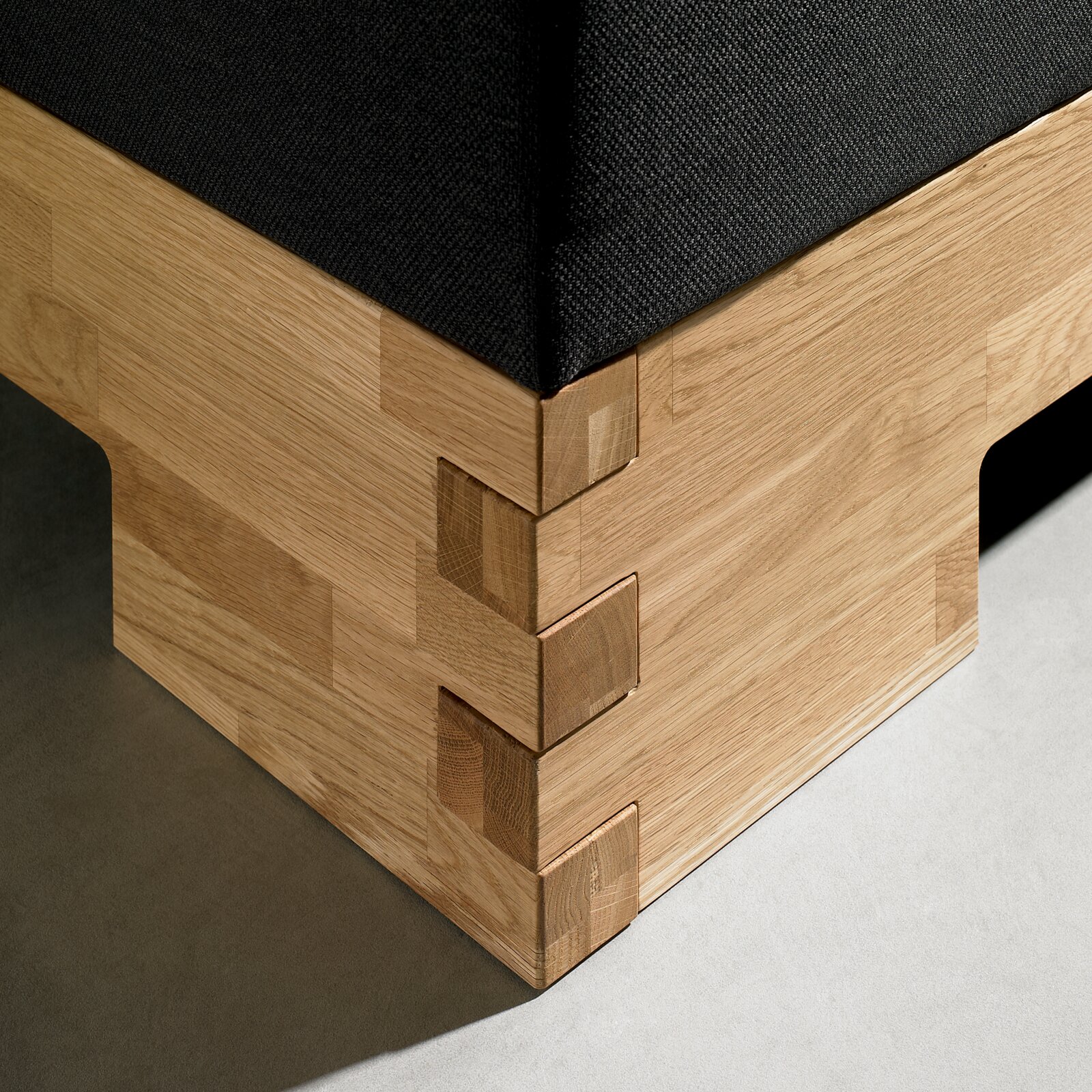Detailansicht einer Ecke eines Boxspringbetts mit Holzverkleidung und dunklem Stoffbezug.