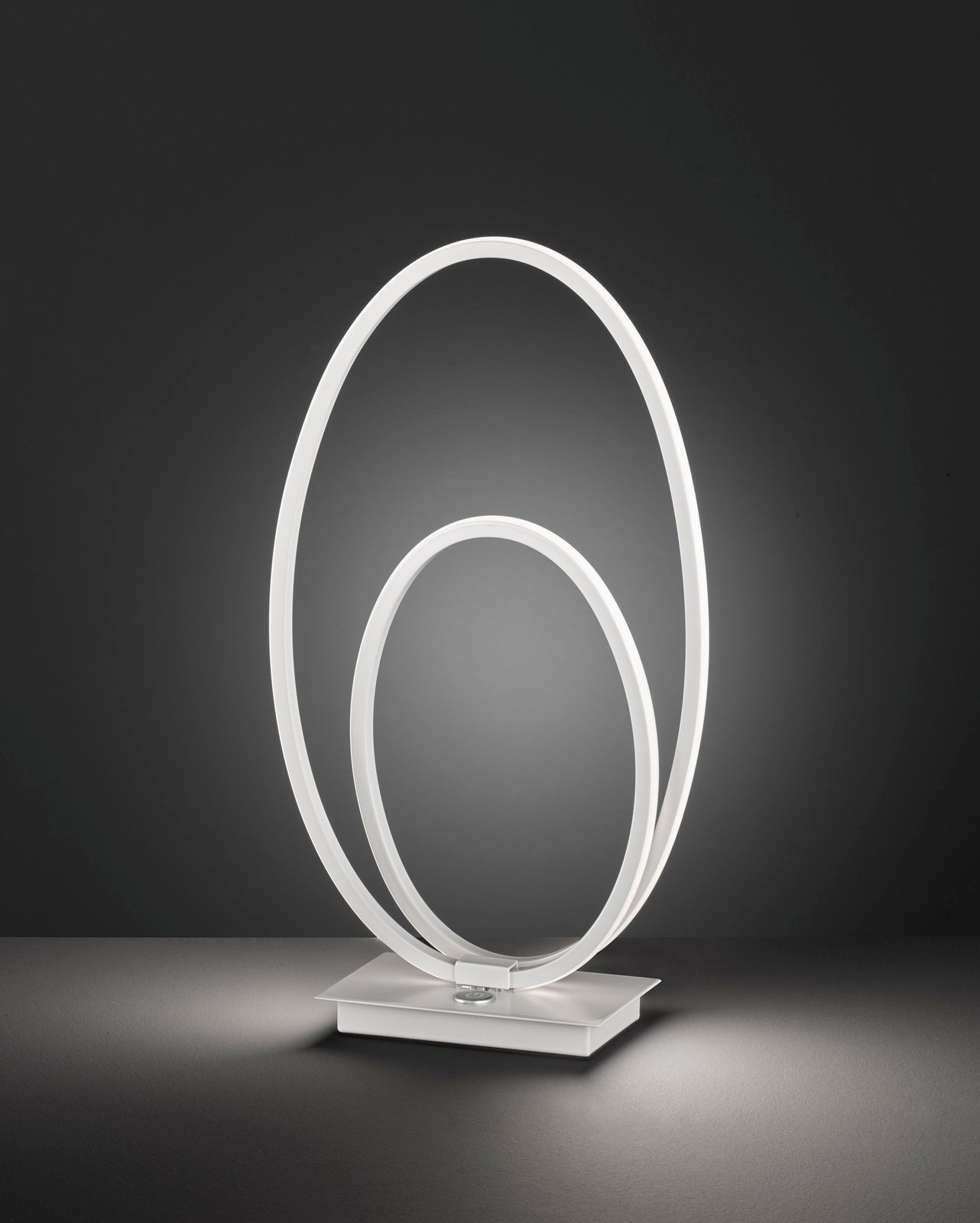 Moderne Tischleuchte mit zwei ineinander verschlungenen, leuchtenden Ringen auf quadratischer Basis, seitliche Perspektive.