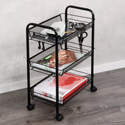 Zwarte metalen rolwagen met drie gaasmanden en wielen, gevuld met boeken en kleine accessoires, gefotografeerd in schuin vooraanzicht in een interieur.