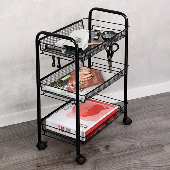 Zwarte metalen rolwagen met drie gaasmanden en wielen, gevuld met boeken en kleine accessoires, gefotografeerd in schuin vooraanzicht in een interieur.
