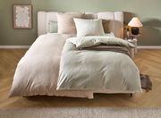 Wendebettwäsche in sanften Beige- und Grüntönen auf einem Bett, mit Kissen und einer gemütlichen Atmosphäre, aus der Perspektive von vorne fotografiert.