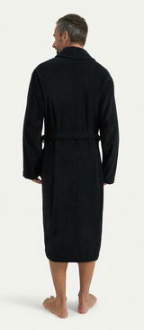 Rückansicht eines schwarzen Bademantels mit Schalkragen, getragen von einer Person. Der Bademantel hat einen Gürtel und reicht bis zu den Waden.