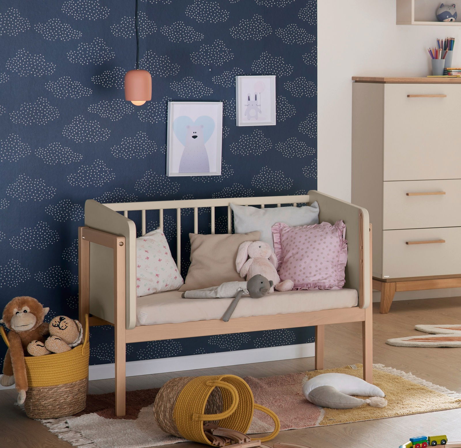 Anstellbett in einem Kinderzimmer, seitliche Perspektive, umgeben von Kissen und Spielzeug.