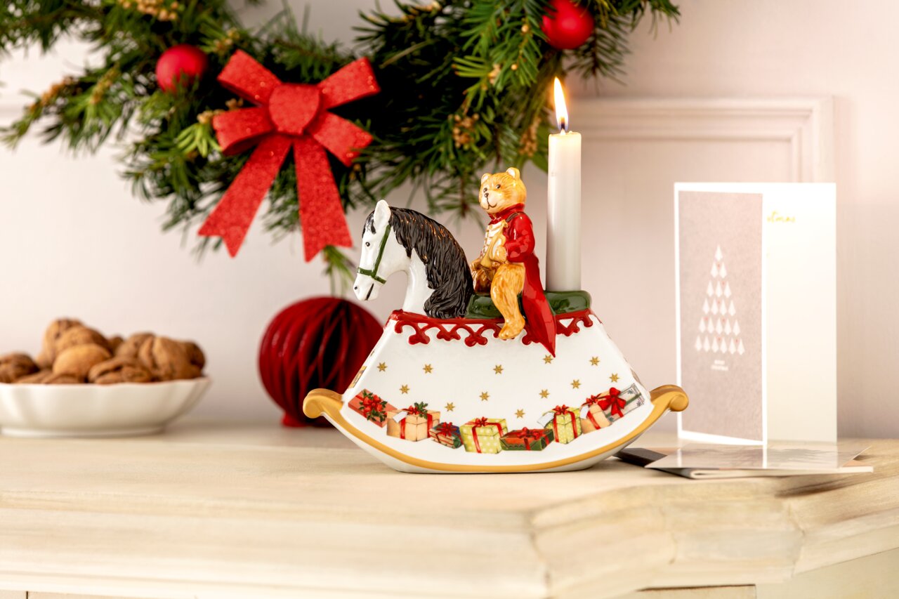 Weihnachtliche Dekoration in Form eines Schaukelpferds mit einem Bären in rotem Mantel und einer brennenden Kerze, seitliche Perspektive.