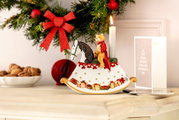 Weihnachtliche Dekoration in Form eines Schaukelpferds mit einem Bären in rotem Mantel und einer brennenden Kerze, seitliche Perspektive.