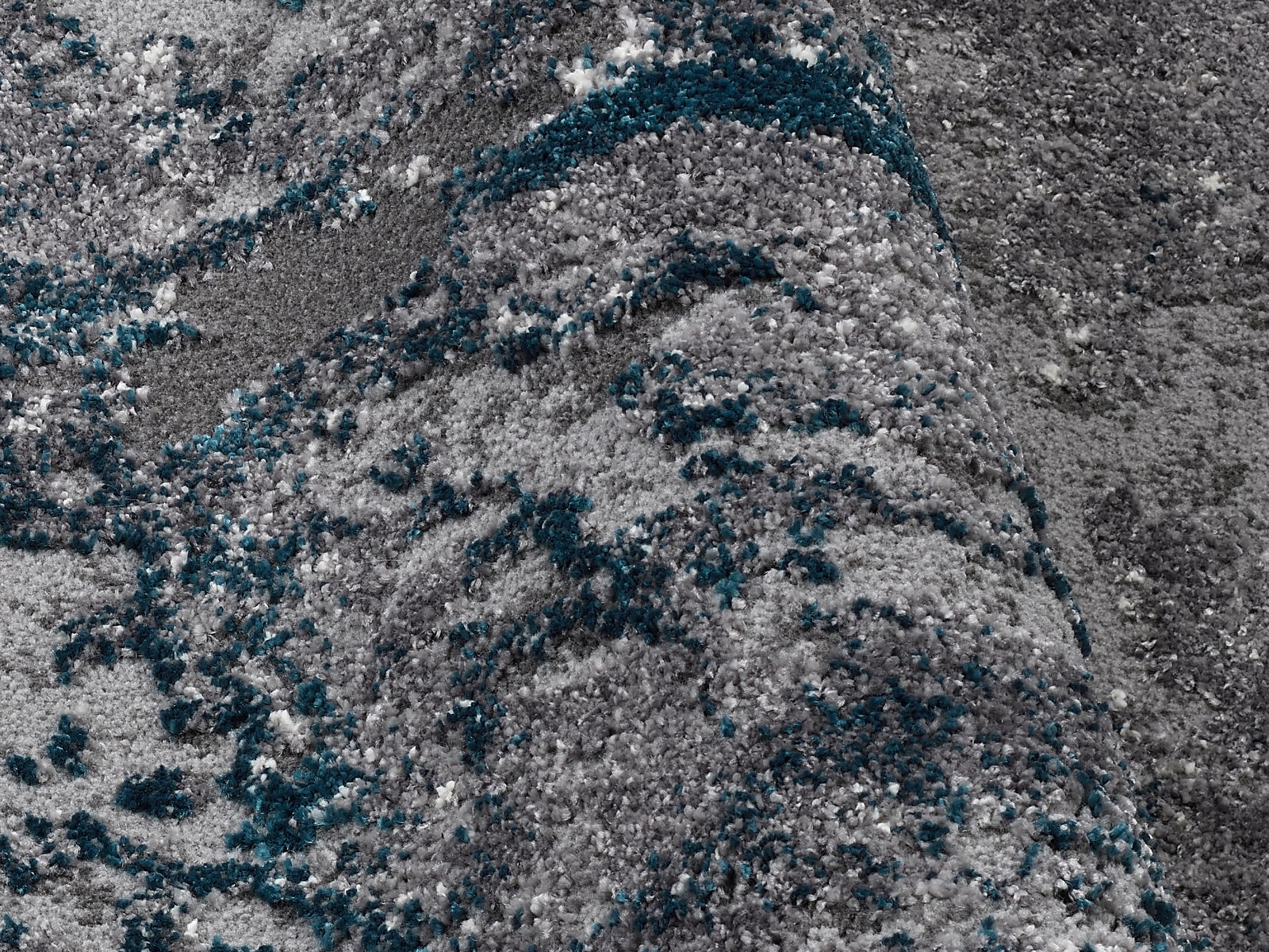 Nahaufnahme eines grauen Teppichs mit blauen und weißen Akzenten, perspektivisch von der Seite aufgenommen.