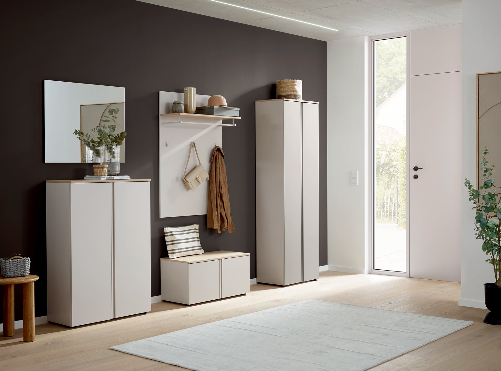 Voleo Bank MILTON Modernes Garderoben-Set im Flur mit weißen Schränken, Garderobenpaneel mit Haken und Ablage sowie Sitzbank, seitliche Perspektive in einem hellen Eingangsbereich mit dunkler Akzentwand und großer Glastür.