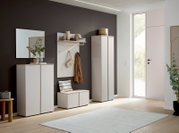 Modernes Garderoben-Set im Flur mit weißen Schränken, Garderobenpaneel mit Haken und Ablage sowie Sitzbank, seitliche Perspektive in einem hellen Eingangsbereich mit dunkler Akzentwand und großer Glastür.