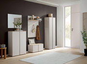 Moderne garderobeset in de hal met witte kasten, een garderobepaneel met haken en een legplank, en een bankje; zijaanzicht in een lichte hal met een donkere accentmuur en een grote glazen deur.