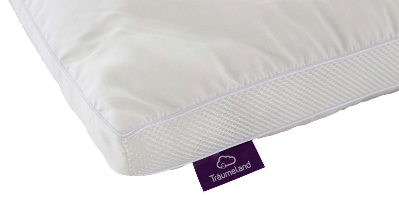 Nahaufnahme eines weißen Kinderkissens mit atmungsaktiver Netzstruktur an der Seite und einem lila Etikett mit der Aufschrift 'Träumeland'.