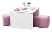 Kindertisch mit weißer Oberfläche, umgeben von zwei rosa gepolsterten Hockern, aus der Perspektive von schräg oben. Auf dem Tisch befinden sich bunte Stifte, Papier und ein Glas.