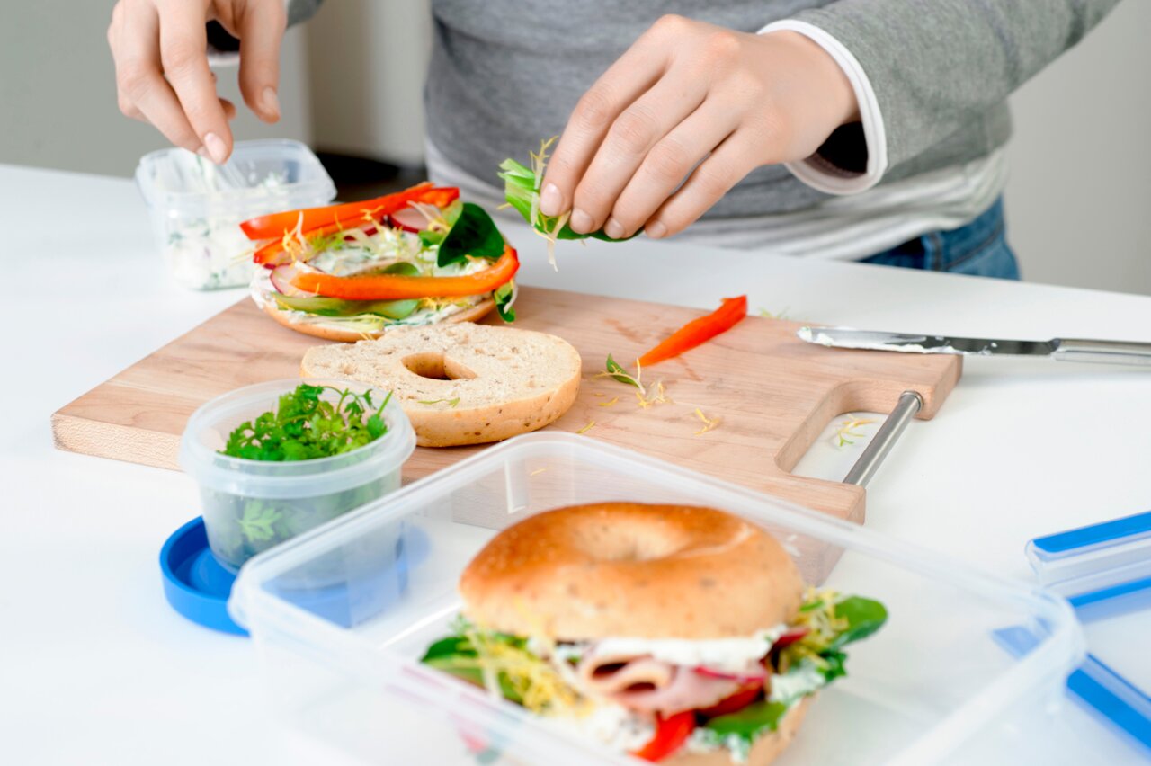 Emsa Frischhaltedose CLIP & CLOSE Frischhaltedose mit frischen Kräutern auf einem Tisch, im Hintergrund ein belegter Bagel auf einem Schneidebrett, Perspektive von oben