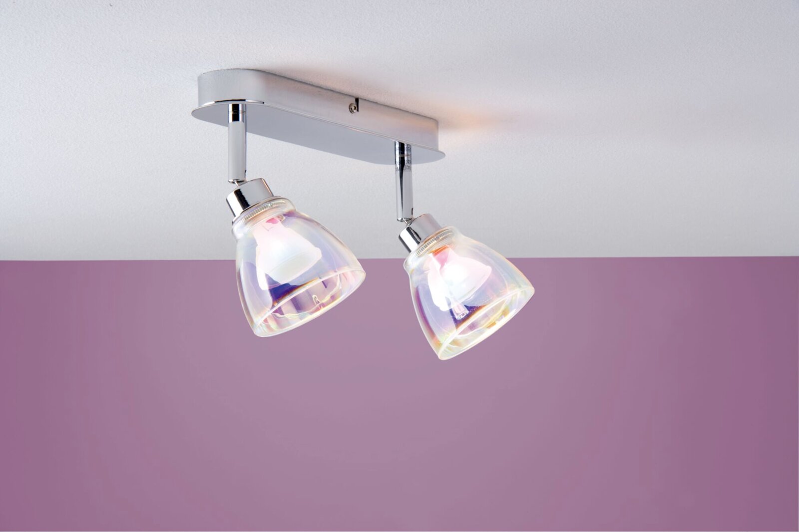 Plafondlamp met twee lampen en draaibare, iriserende glazen kappen, van onderaf gezien tegen een paarse muur.