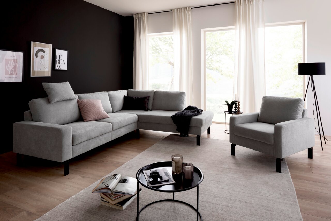 Grauer Sessel in modernem Wohnzimmer mit Ecksofa, Couchtisch und großen Fenstern, seitliche Perspektive.